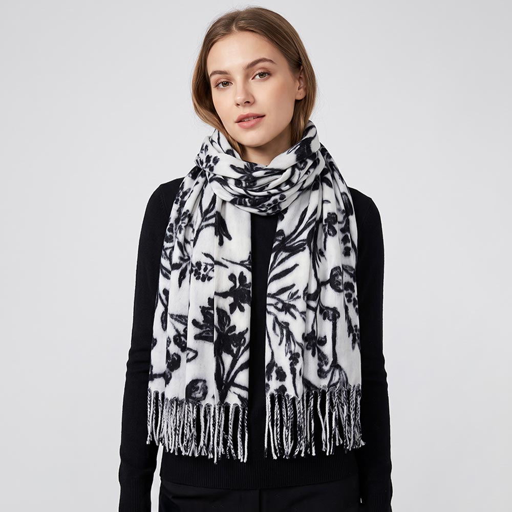Woman wearing black and white botanical floral print pashmina scarf looped around neck over black sweater