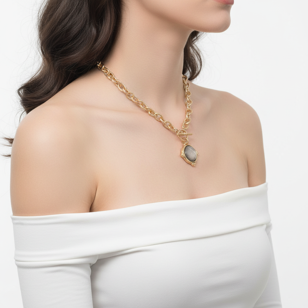 Model wearing gold tone rope chain toggle necklace with grey stone pendant, over-shoulder view, white off-shoulder top, white background