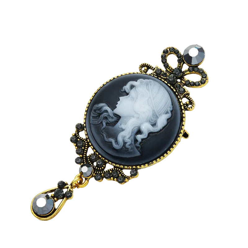 Vintage cameo bow drop brooch styled on a white dish, angled view highlighting gold filigree and black crystals