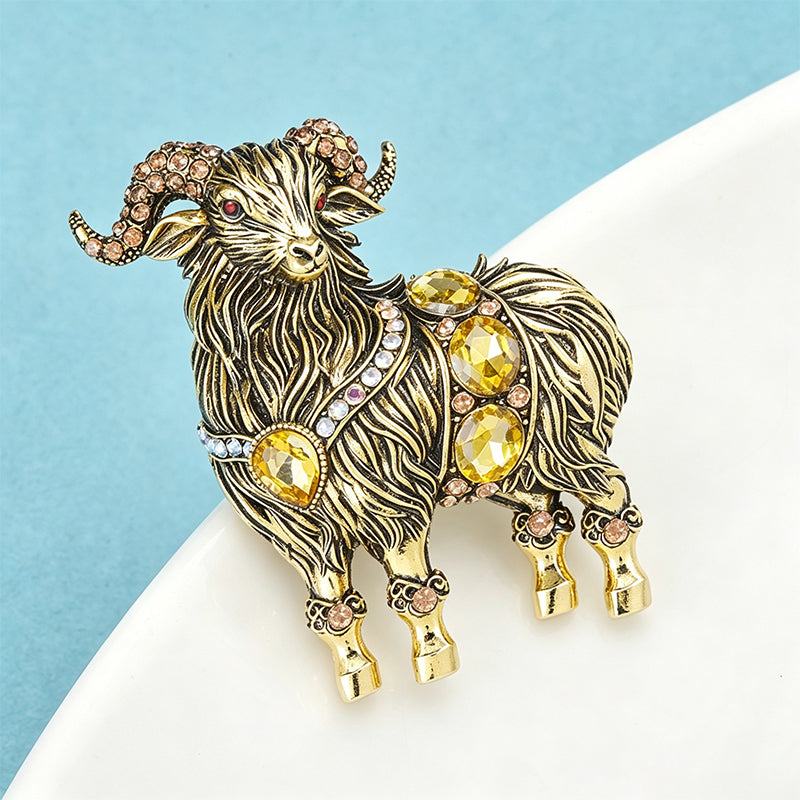 Antique gold ram brooch with faceted citrine crystals and pink rhinestone accents on white surface