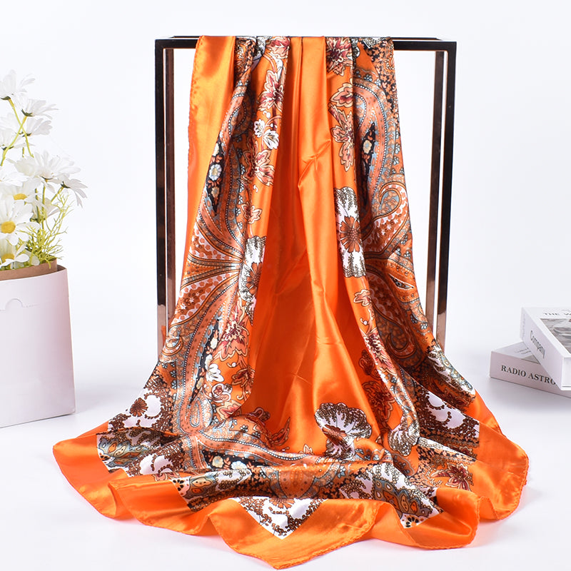 Orange paisley floral silk-feel square scarf draped on display stand showing fluid satin drape