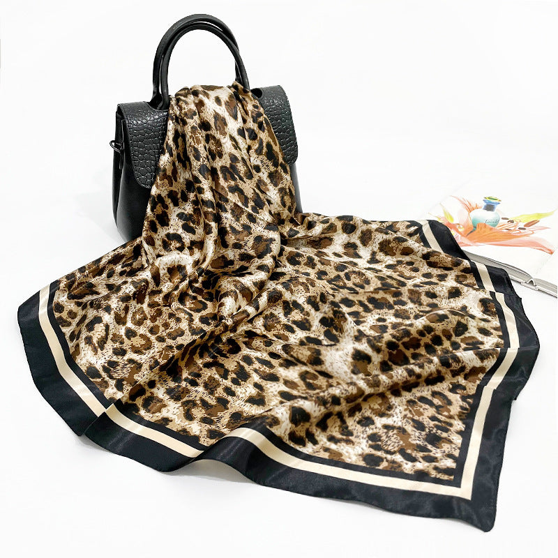 Silk-feel leopard print square scarf draped over black leather handbag, showing full pattern and black ivory border