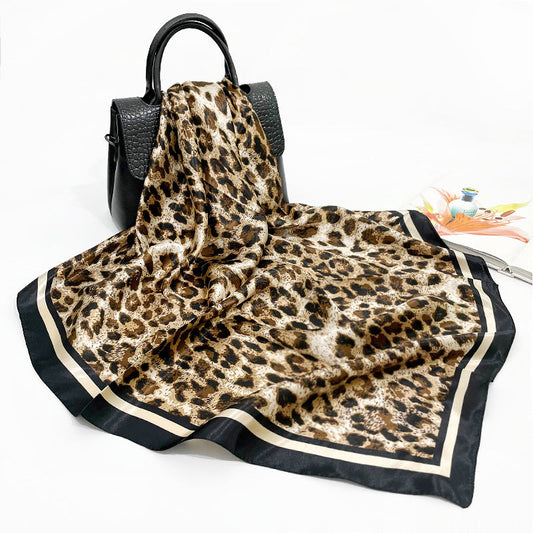 Silk-feel leopard print square scarf draped over black leather handbag, showing full pattern and black ivory border
