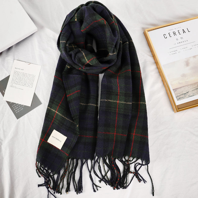 Navy green tartan plaid scarf with knotted fringe tassel trim laid flat on white surface
