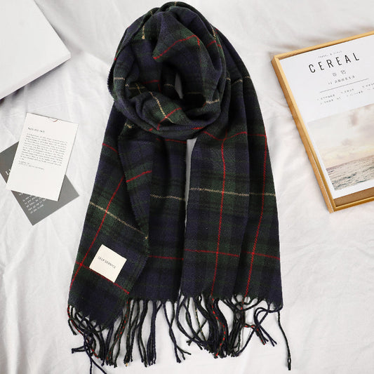 Navy green tartan plaid scarf with knotted fringe tassel trim laid flat on white surface