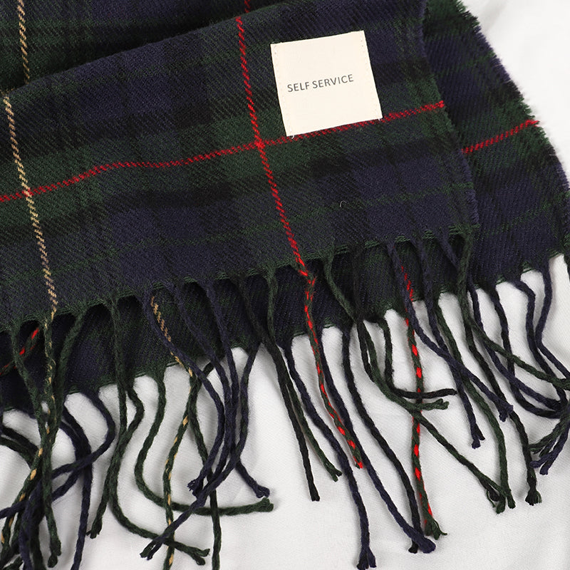Detail shot of navy tartan scarf corner showing knotted fringe tassels and Self Service label