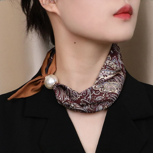 Woman wearing burgundy paisley neckerchief with pearl clasp over black blazer – neck detail