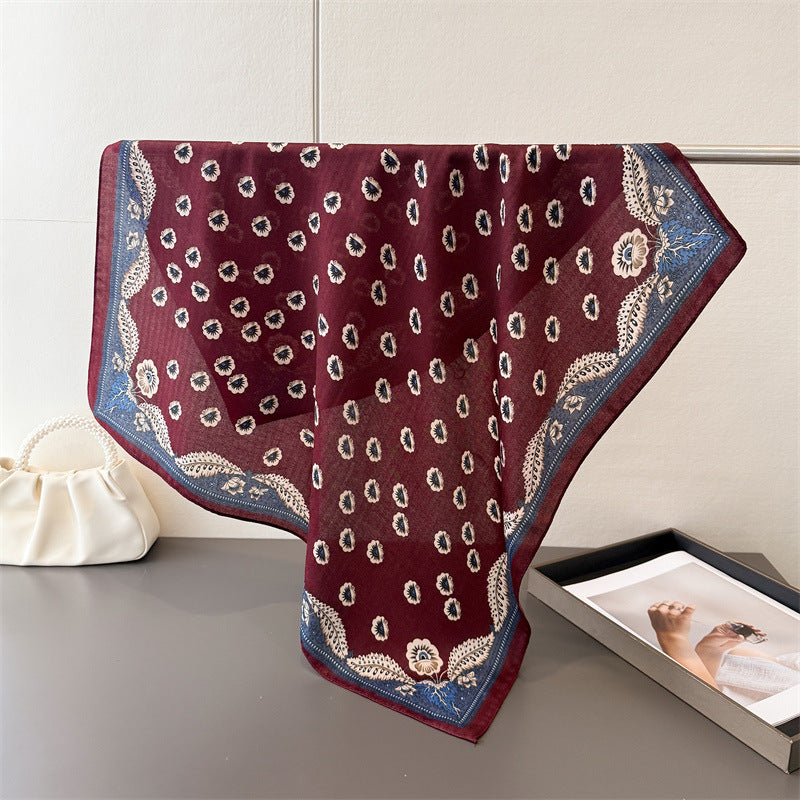 Close-up of burgundy cotton-blend scarf rolled to show cream and navy floral motif texture and fabric softness