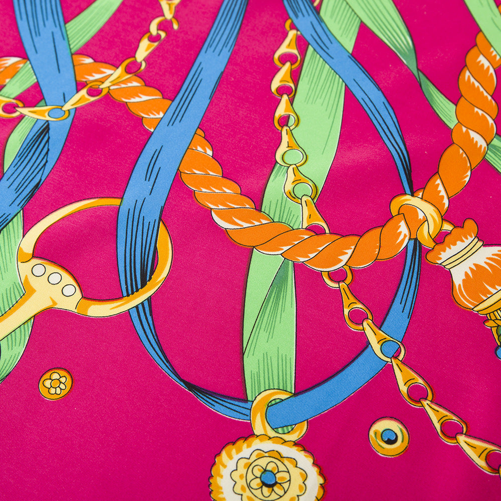Fuchsia silk scarf folded into square showing ribbon and gold pendant detail