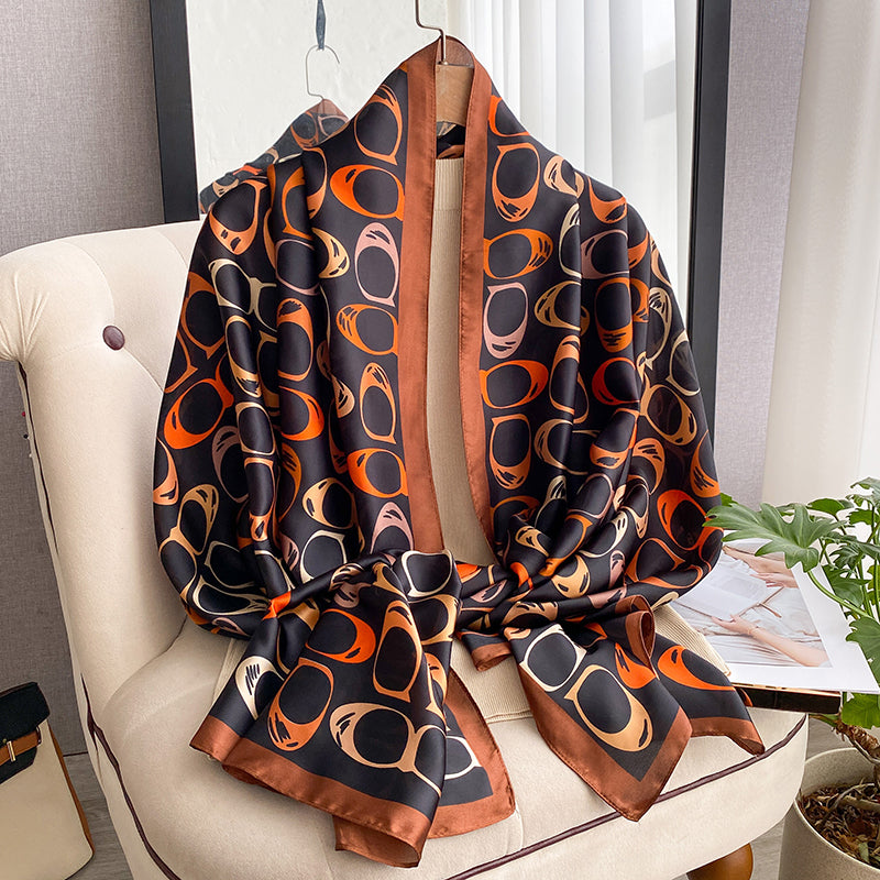 Retro abstract sunglasses print silk-feel wrap scarf in black and burnt orange draped over a chair