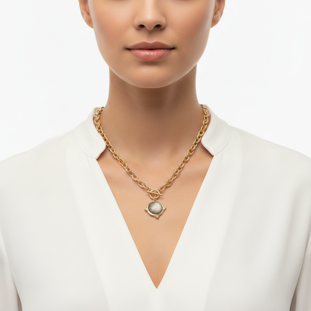 Model wearing gold tone rope chain toggle necklace with grey stone pendant, front view, white blouse, white background